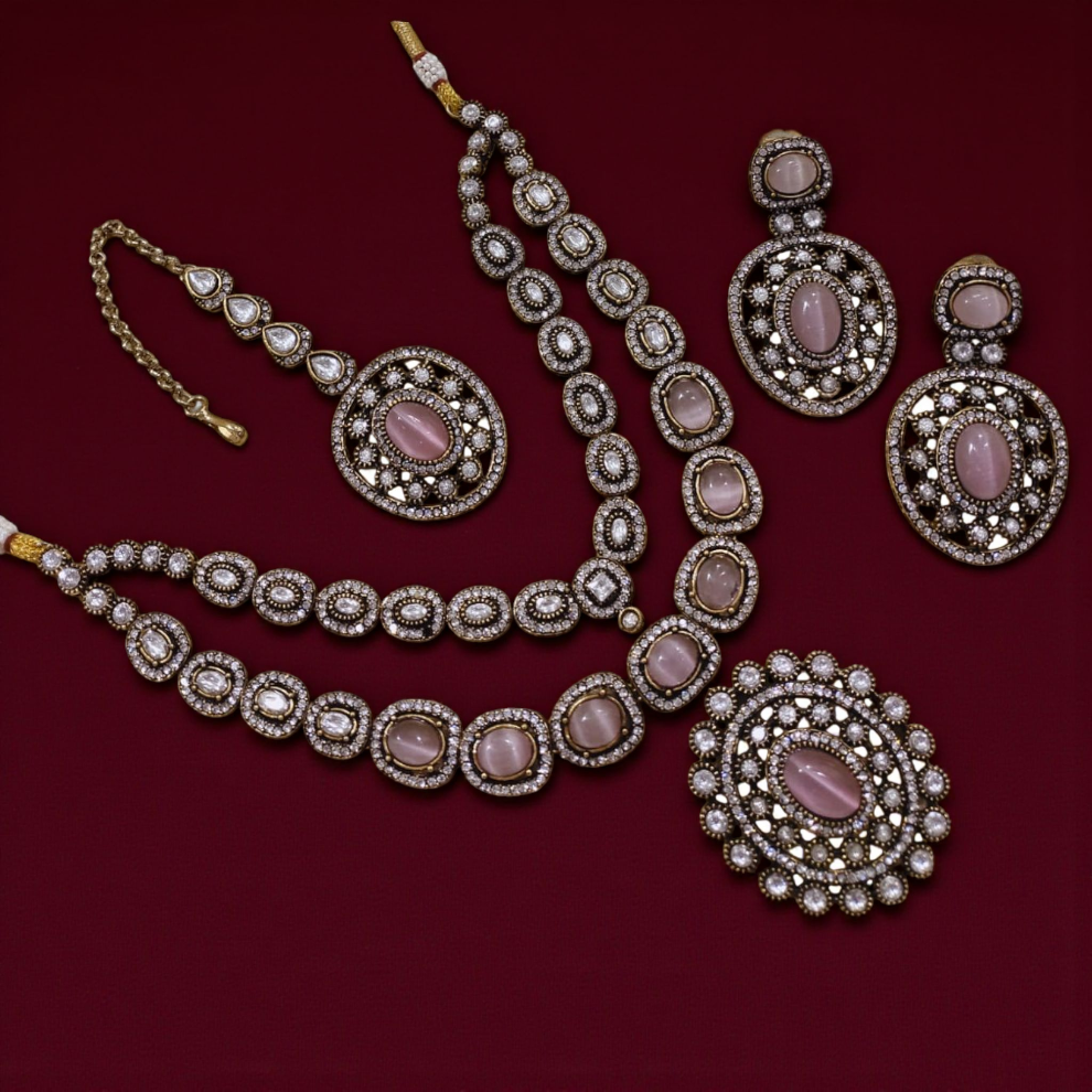 Elegant Kundan jewelry set featuring pink oval gemstones with intricate diamond detailing, including a necklace, maang tikka, earrings, and a statement pendant