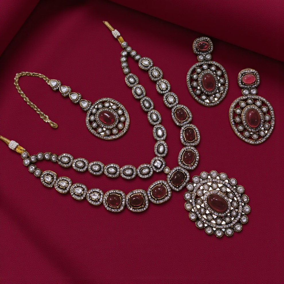 Luxurious maroon stone-studded Kundan jewelry set with intricate white crystal work, including a necklace, oversized earrings, a pendant, and a maang tikka.