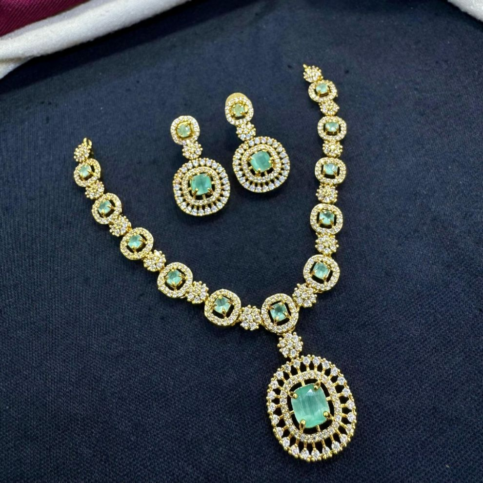Elegant gold necklace set adorned with  sea-green gemstones and intricate diamond detailing, paired with matching drop earrings.
