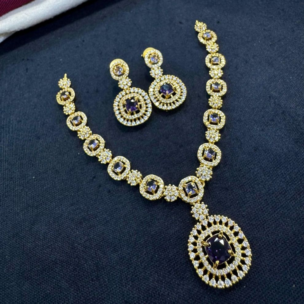 Glamorous gold necklace set embedded with rich blue gemstones in a symmetrical design, paired with double-hoop style earrings